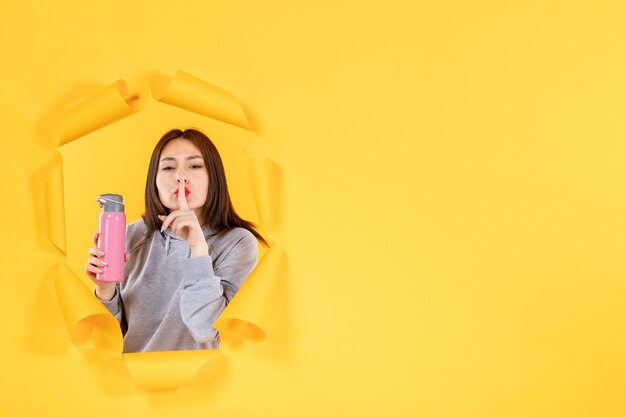 Hembra joven con una botella de agua sobre papel amarillo rasgado gimnasio ajuste atleta de interior de fondo