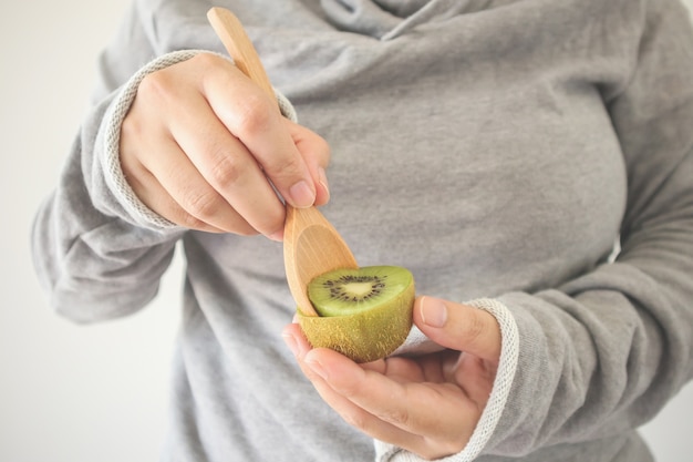 Hembra joven comiendo kiwi maduro con cuchara de madera