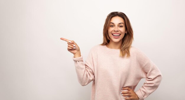 Hembra joven contenta que señala lejos y que sonríe felizmente contra el fondo blanco