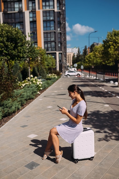 Hembra joven con maleta usando celular al aire libre