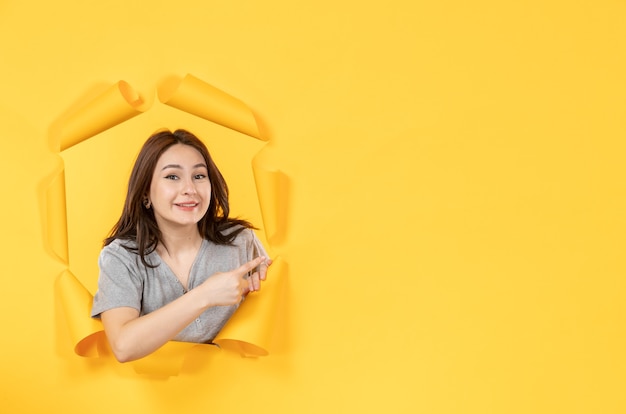 Hembra joven mirando a través de un agujero en el fondo de papel amarillo mirar publicidad en la ventana