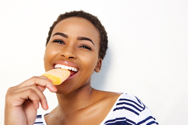 Hembra joven negra comiendo helado contra la pared blanca