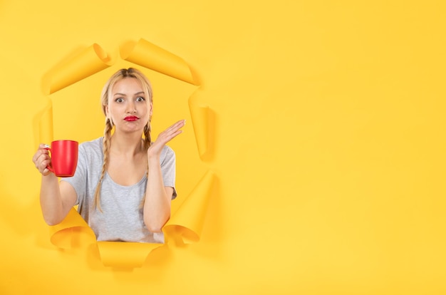 Hembra joven con taza de té sobre fondo de papel amarillo publicidad comercial