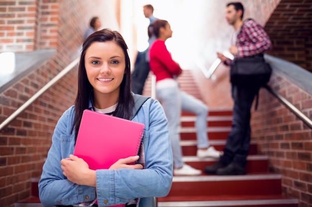 Hembra que sostiene los libros con los estudiantes en las escaleras en la universidad