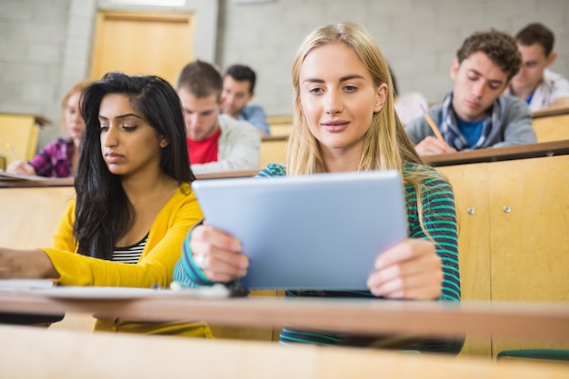 Hembra que usa la PC de la tableta con los estudiantes en la sala de conferencias