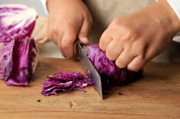 Hembra rebanar repollo morado en una tabla de cortar de madera