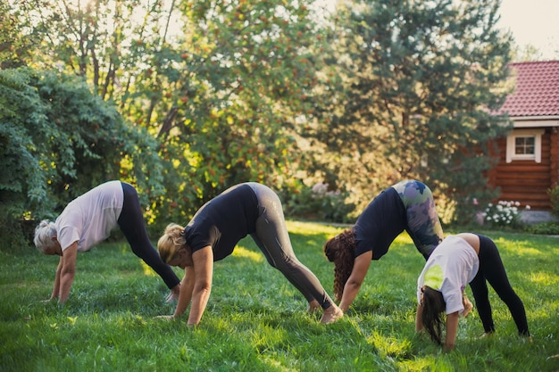 Hembras activas de diferentes generaciones de familia haciendo ejercicio juntas estirando la espalda y las piernas