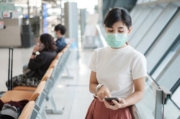 Las hembras jóvenes con mascarilla y con smartphone móvil en el aeropuerto