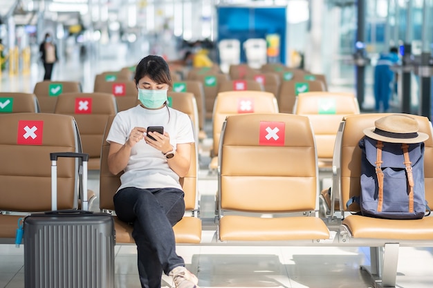 Las hembras jóvenes con mascarilla y con smartphone móvil en el aeropuerto