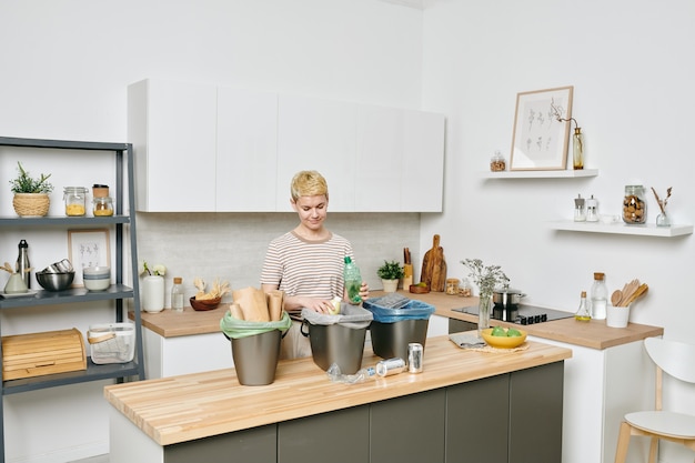 Las hembras jóvenes de pie junto a la mesa de la cocina mientras clasifica los residuos