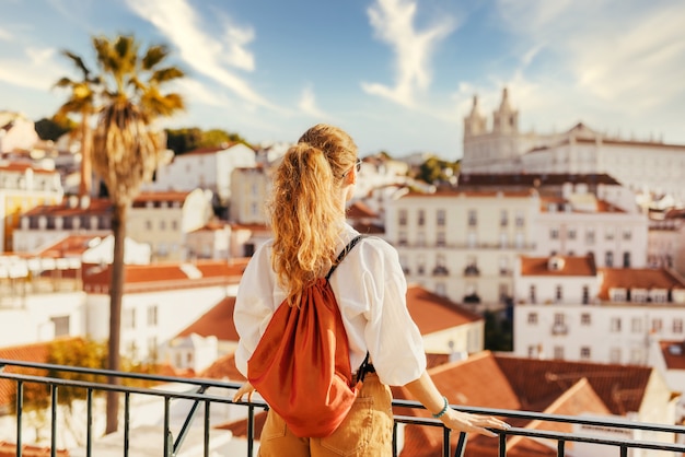 Las hembras jóvenes de pie sobre una plataforma rodeada de vallas y observando Lisboa durante el día en Portugal