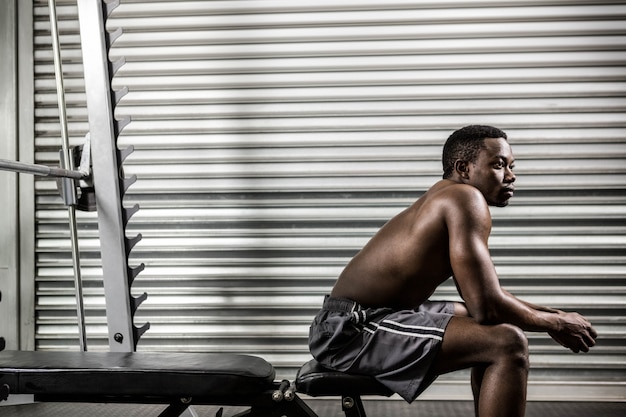 Hemdloser Mann, der auf Bank an der crossfit Turnhalle sitzt