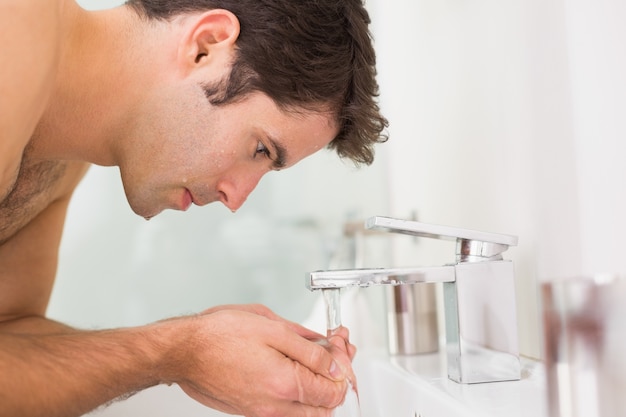 Hemdloses waschendes Gesicht des jungen Mannes im Badezimmer