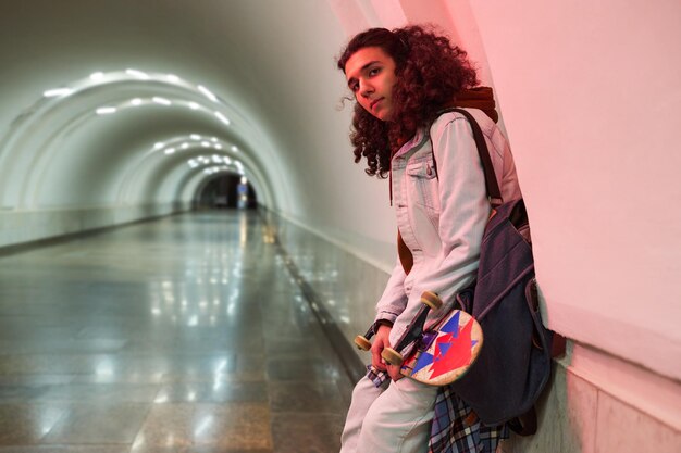 Heranwachsender Mann in stylischer Freizeitkleidung hält Skateboard in der Hand, während er an der Wand steht