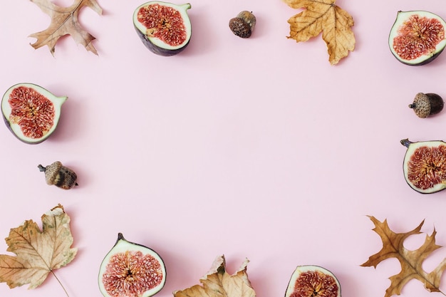 Herbst-Fall-Zusammensetzung von reifen lila Feigen Frisches Obst bunte Ahorn- und Eichenblätter und Eicheln isoliert auf rosa Hintergrund Dekoratives florales Rahmenmuster Flache Ansicht von oben Erntegrenze