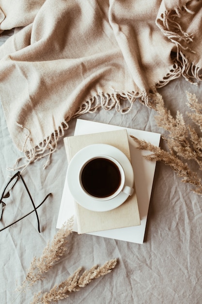 Herbst, Herbst Komposition. Eine Tasse Kaffee auf dem grauen Leinenbett mit beiger warmer Decke, Büchern, Gläsern und Schilf
