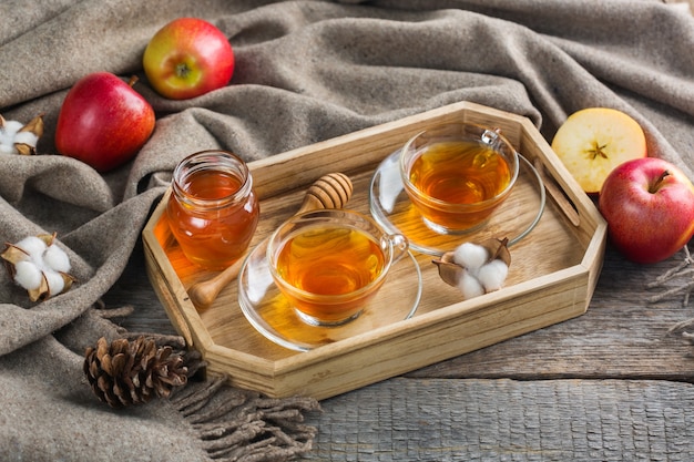 Herbst, Herbst, Winter Wohnkultur im Hygge-Stil mit Getränk. Saisonale Komposition mit Tasse heißem Tee mit Honig, warmem Wollschal, weichem Plaid auf einem rustikalen Holztisch.