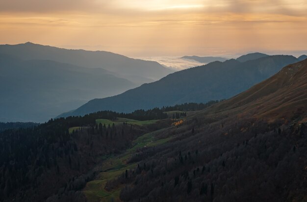 Herbst im Nordkaukasus, Skigebiet Rosa Khutor in der Nebensaison. Russland, Sotschi. Vintage-Tönung. Reise-Hintergrund. Landschaft mit Sonnenlicht, das durch orangefarbene Wolken und Nebel scheint.