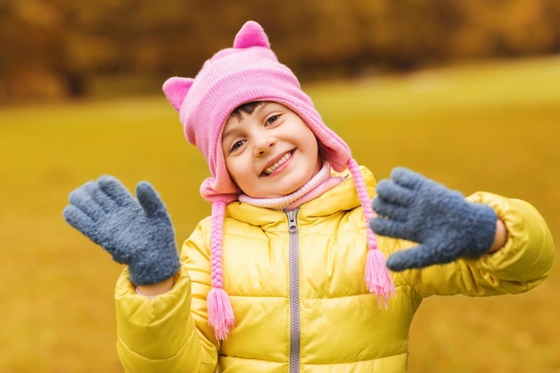 herbst, kindheit, glück und personenkonzept - glückliches schönes kleines mädchen, das draußen hände winkt