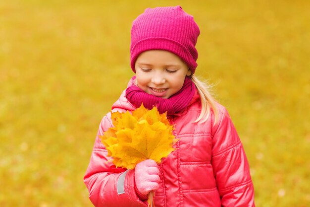 Herbst-, Kindheits-, Glücks- und Menschenkonzept - glückliches schönes kleines Mädchen mit Ahornblättern im Freien