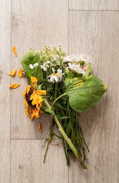 Herbst-Konzept. Ein Strauß verwelkter Blumen und eine Sonnenblume auf dem Boden. Flach legen