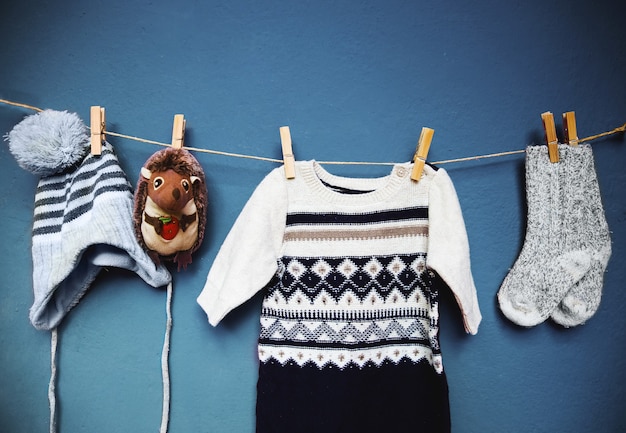 Herbst- oder Winterkleidung für Kinder, die an der Wäscheleine auf einem strukturierten Wandhintergrund hängt