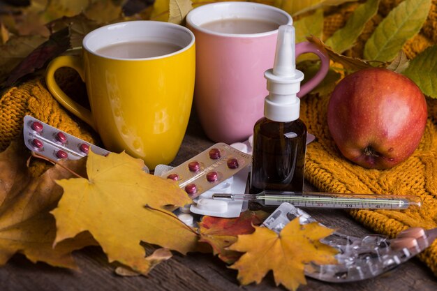 Herbst und Gesundheitsvorsorge. Erkältung und Grippe. Tasse Tee, Pillen und Thermometer auf Holzuntergrund