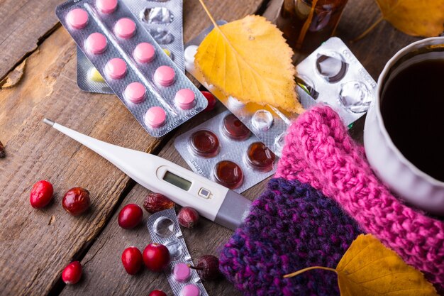 Herbst und Gesundheitsvorsorge. Hausapotheke - Tasse Tee, Pillen und Thermometer auf Holzhintergrund