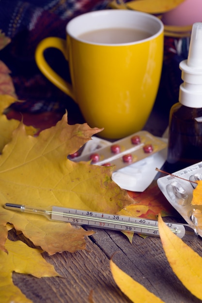 Herbst und Gesundheitsvorsorge. Tasse Tee, Pillen und Thermometer auf Holzuntergrund