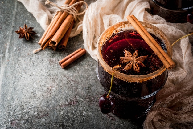 Herbst- und Wintergetränke. Heiße Kirschsangria mit Zimt, Anis, Wein und Gewürzen. Auf einem dunklen Stein und Holz mit Zutaten,