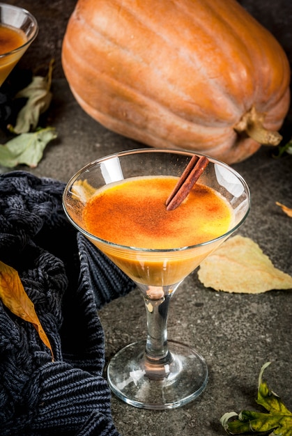 Herbst- und Wintergetränke. Thanksgiving- und Halloween-Cocktails. Kürbiskuchen Margarita mit Zimtstange, auf schwarzer Steintabelle. Gemütliches Zuhause, mit Herbstlaub, Plaid, Kürbis, Kopienraum