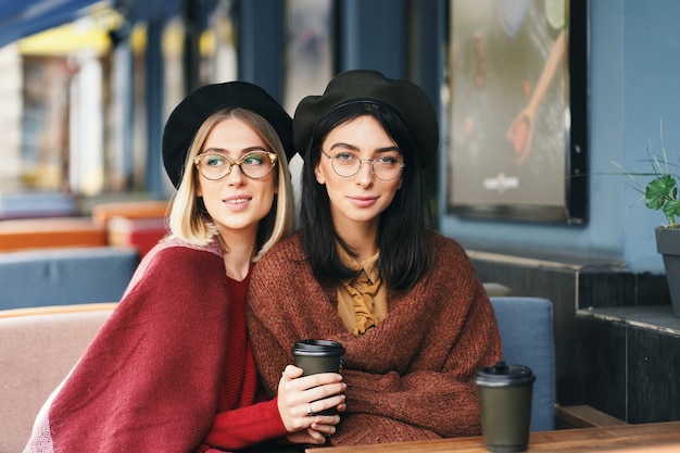 Herbst-Winter-Porträt von zwei jungen Frauen in einem Straßencafé, Kaffee zu trinken, zu sprechen.