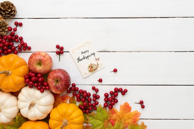 Herbstahornblätter mit Kürbis und roten Beeren auf weißem hölzernem. Erntedankfest-Konzept