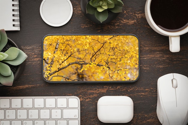 Herbstarbeit im Büro aus der Ferne oder Arbeit zu Hause Fernunterricht im Herbstlaub auf dem Telefonbildschirm, umgeben von Büroartikeln, Tastatur und Kopfhörern