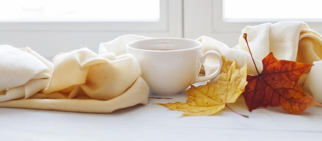 Herbstblätter mit einer Tasse Tee oder Kaffee neben einem Schal auf einem hölzernen Hintergrundbanner