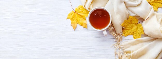 Herbstblätter mit einer Tasse Tee oder Kaffee neben einem Schal auf einem hölzernen Hintergrundbanner