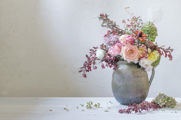 Herbstblumen und -beeren im rustikalen keramischen Krug auf weißer Hintergrundwand