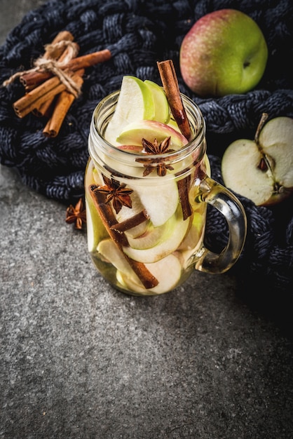 Herbstcocktail. Hineingegossenes Diätentgiftungswasser mit Apfel- und Gewürzanis, Zimt. Alkoholcocktail mit Apfelwein. Im Einmachglas auf einem schwarzen Steintisch.