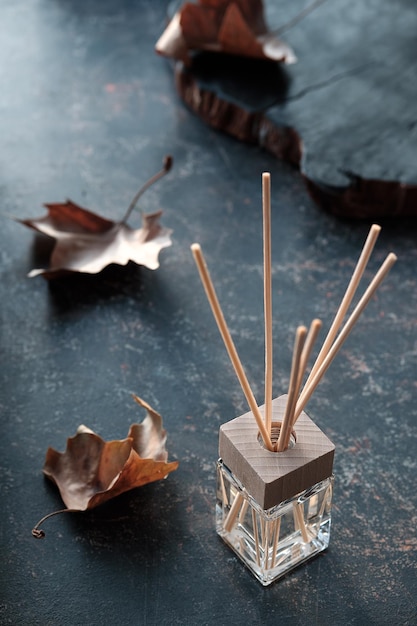 Foto herbstduftkonzept bamboo sticks diffusor duftende lufterfrischerflüssigkeit in glasfläschchen mit holzplatte hygge-duft aromatherapie-wellnesskonzept retro-getönter dunkelbrauner strukturierter hintergrund