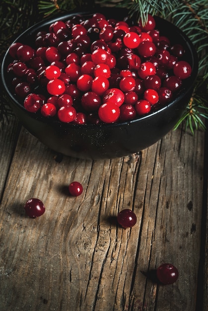 Herbsternte, saisonale Beeren. Frische rohe Cranberries in einer schwarzen Schale, mit Ästen, auf einem alten Holztisch,