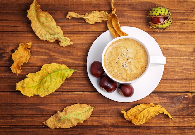 Herbstgelbe Blätter, Kastanien und eine Tasse Kaffee auf Holzhintergrund.