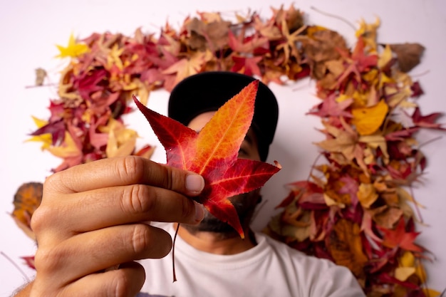 Herbsthintergrund Mann mit schwarzer Mütze in einem Studio, der mit einem roten Blatt in der Hand liegt