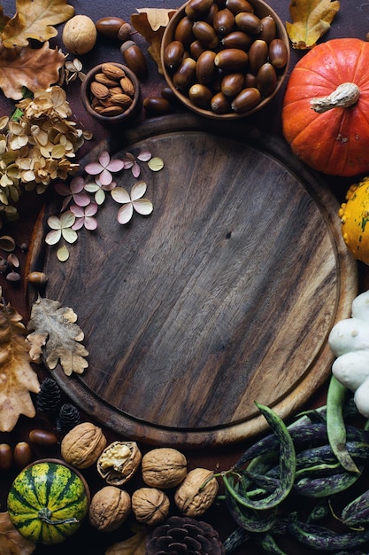 Herbsthintergrund mit dekorativen Kürbiseicheln, Nüssen, Grüns, Herbstlaub und Holzbrett mit Platz für Text auf dunklem Steintisch, Ernten Sie Stillleben, Zusammensetzung, Thanksgiving-Hintergrund