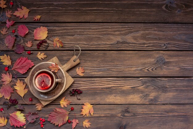 Herbsthintergrund mit Kopienraum. Tee mit Zitrone, Blättern und Beeren auf einem Holztisch.