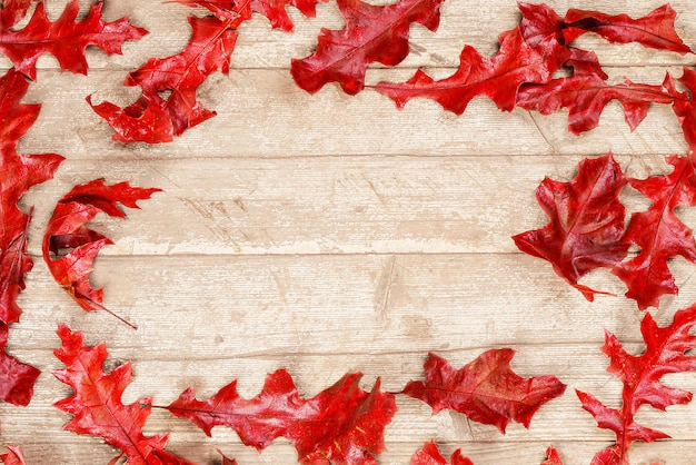 Herbsthintergrund von roten Eichenblättern auf einer Holzoberfläche der ursprünglichen Farbe. Rote getrocknete Blätter auf rustikaler Oberfläche