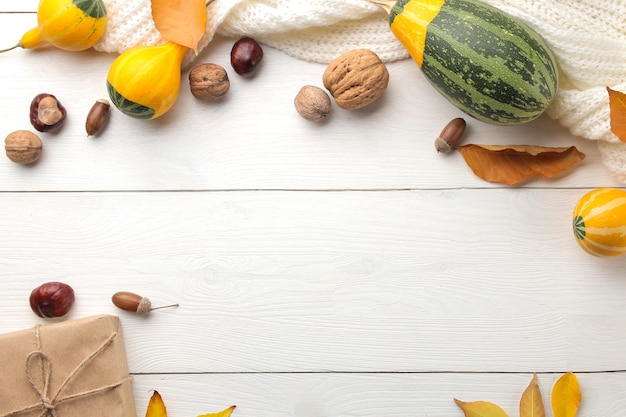 Herbstkomposition mit dekorativen Kürbissen und gelben Blättern und einem warmen Schal. Herbstzeit. auf einem weißen Holztisch. Draufsicht mit Platz für Beschriftung