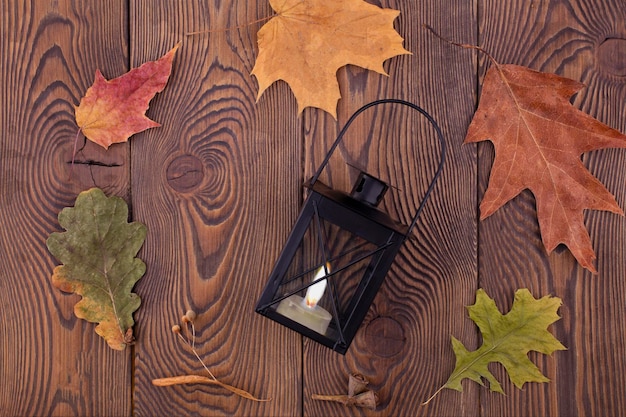 Herbstkomposition mit einer Kerzenleuchter-Laterne in der Mitte Herbsttrockene Blätter auf einem Holzhintergrund im rustikalen Stil Flacher Kopienraum