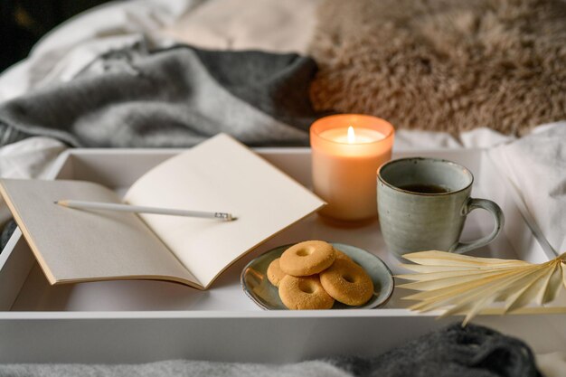 Herbstkomposition mit einer Tasse Kaffee, Kerze, Kekse, Notizbuch, Bleistift im bequemen Bett