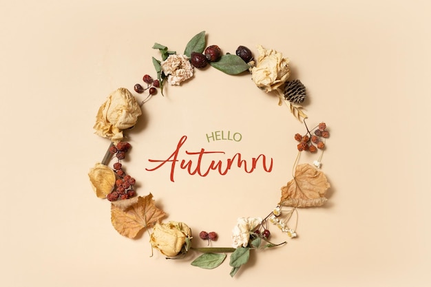 Herbstkomposition mit Hello Autumn Text Kranz aus getrockneten Blättern und Blumen auf Pastellbeige