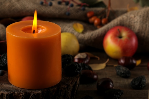 Herbstkomposition mit Kerzen und Herbstfrüchten und Beeren und Kastanien auf einem braunen Holztisch